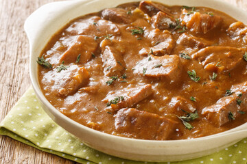 Beef stew in dark beer with onions, spices and thyme close-up in a saucepan on the table. horizontal