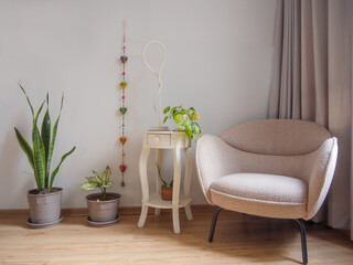 Elegante mueble de lectura beige, acompañado de maceteas con plantas y mesa blanca con lampara y adornos con fondo blanco y cortinas grises