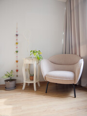 Elegante mueble de lectura beige, acompañado de maceteas con plantas y mesa blanca con lampara y adornos con fondo blanco y cortinas grises