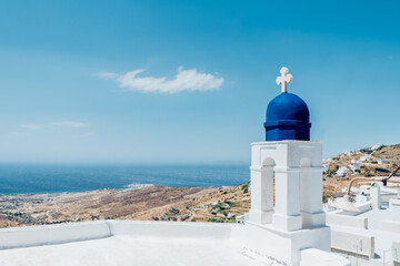 Top of traditional church in Tinos, Greece with blue roof top and cross with blue sky background