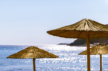 Straw beach umbrellas with sea and blue clear sky on background, concept of sun protection during summer vacation