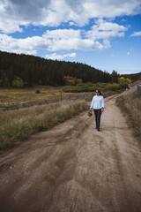 Woman walking along a dirt road wearing a white sweater - rural setting - nature and sustainability - harvest and fall