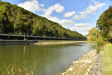 Fototapeta na wymiar La Meuse avec voie de circulation routière entre les hautes collines boisées à Lustin au sud de Namur
