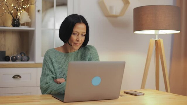 Attractive middle-aged woman using a laptop computer sitting at the workplace hacking. Happy businesswoman executive worker working typing on computer at home
