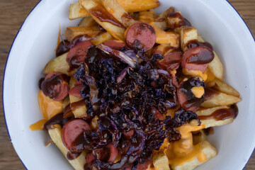 Food background. Closeup view of fried potatoes with sausages, red cabbage, cheddar cheese and barbecue sauce, in a white bowl.
