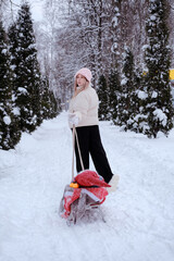 Mother or girl or woman walking in the forest in winter with sledges and white winter landscape on background