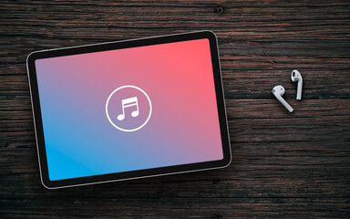 Music note logo on blue to pink gradient screen of tablet and wireless earphones on dark wooden surface. Music streaming