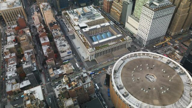 Fly above Madison Square Garden and Moynihan Train Hall. Vehicles driving on streets in city. New York City, USA