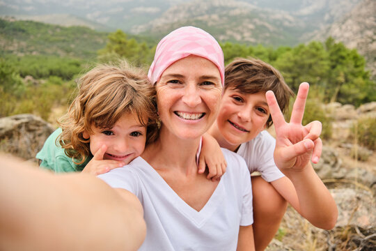 A woman with cancer taking a selfie with her family in the mountains.