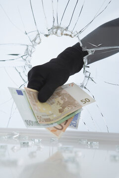 Hand Stealing Money Through Broken Glass