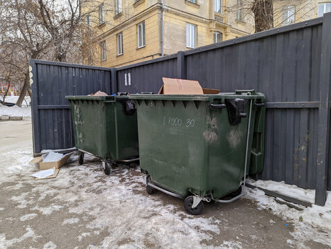 Green plastic containers for garbage collection in the yard of an old multi-storey residential building. Dumpster. Winter. Container site.