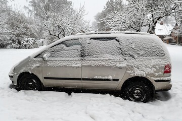 The car in the parking lot is covered with snow.