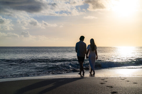 silhouette of young engaged couple holding hands in love during the sunset on a sandy island beach