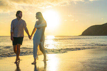 Happy couple walking along waterfront sandy beach on a tropical island during the golden hour