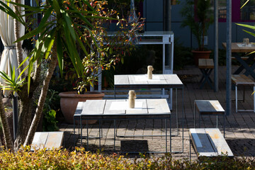 Mehrere Tische stehen auf einer Terrasse, die mit Blumentöpfe und Pflanzen dekoriert ist, und warten auf Gäste.