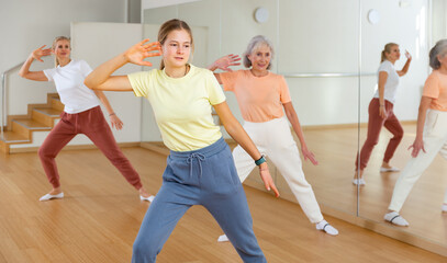 Fototapeta na wymiar Young girl performing aerobic dance during group training with her mother and grandmother.