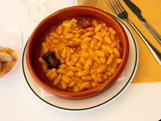 Delicious Fabada asturiana with stewed beans, pork, morcilla and chorizo served in traditional clay...