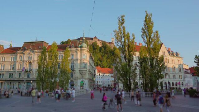 Historical pedestrian street with architectural buildings decorated with red tiles and walking crowd at sunset in Ljubljana Slovenia