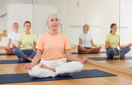 Group of people of different ages sitting in lotus position practicing meditation in yoga class - Powered by Adobe
