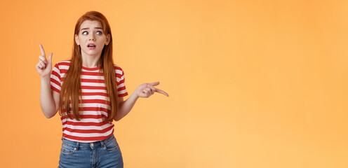 Complicated questioned redhead girlfriend trying understand what happening, which way go, look around, pointing sideways up and right, frowning perplexed, taking hard decision, orange background - obrazy, fototapety, plakaty