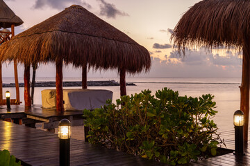 chaises à massage installées sous un toit de paille en bord de mer lors d'un lever de soleil