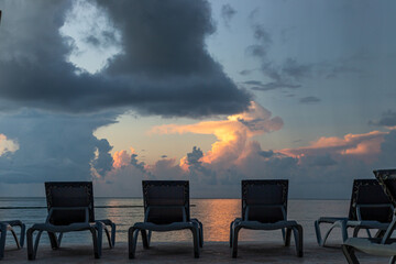 vue sur des chaises installées en rangées au bord d'une piscine près de la mer lors d'un lever de soleil avec des couleurs dans les nuages