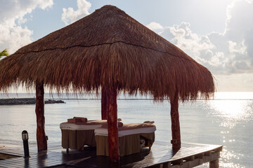 chaises à massage installées sous un toit de paille en bord de mer avec un ciel ensoleillé