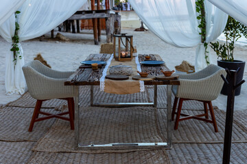 installation extérieur avec une table et des chaises pour une expérience de diner en amoureux sur la plage - obrazy, fototapety, plakaty