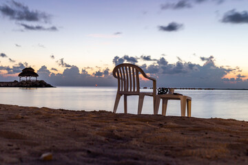 Fototapeta na wymiar chaise en plastique et tabouret sur la plage en bord de mer lors d'un lever de soleil