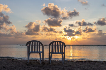 Fototapeta na wymiar pair de chaises en plastique sur la plage avec vue sur la mer lors d'un lever de soleil