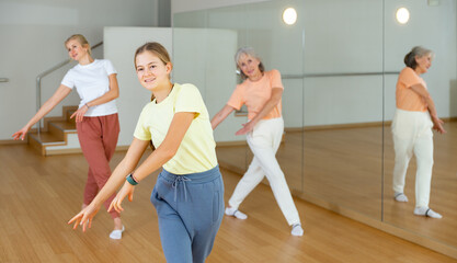 Fototapeta na wymiar Ordinary teen girl with family exercising dance moves with group of people in dance center