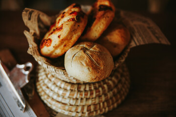 Cesta de mimbre, rellena de panes caseros de ajo y tomate, sobre una mesa de madera.