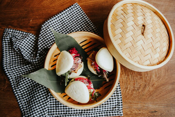 Fotografía de comida emplatada lista para servir, en una cesta de mimbre, decorado con hojas, pan vaho de carne mechada con cebolla.