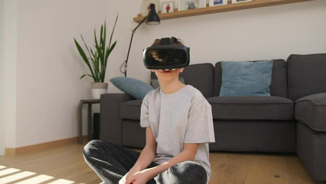 Caucasian school-aged boy enjoying new technology at home, using VR goggles, and interacting with objects in a virtual world, handheld shot.