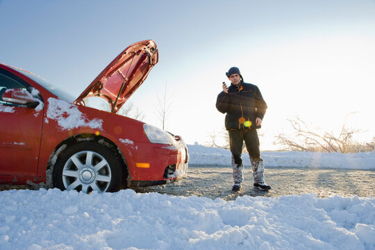 Man Talking on Cell Phone Next to Car with Hood Up in Winter