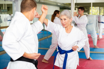 Man and senior woman in kimono sparring during group karate training.