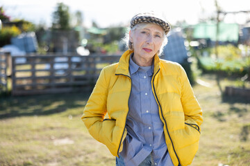 Happy mature European female farmer in yellow zip jacket looking at camera while standing in...