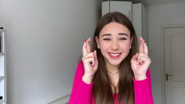 The girl crossed two fingers near her head and is very worried that everything will work out She has emotionally positive emotions sincere smile beautiful teeth long live natural hair pink blouse