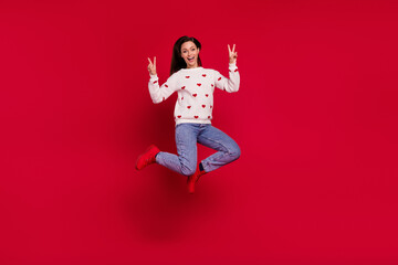 Full length photo of pretty funny girl dressed white pullover jumping high showing two v-signs isolated red color background