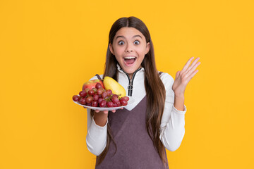 amazed child hold fresh fruit plate on yellow background. vitamins