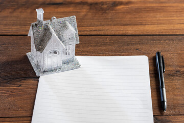 Small house with glitter on a piece of blank paper and wooden table and black pen. Buying dreamy...