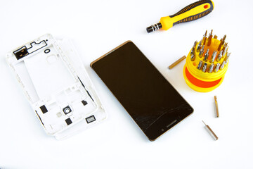 Smartfon z uszkodzonym ekranem i śrubokręty na białym tle. Motyw naprawy smartfona