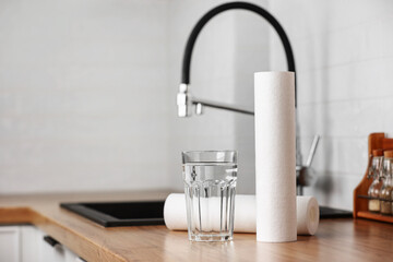 A glass of clean water and foamed polypropylene filter cartridges on wooden table in a kitchen...