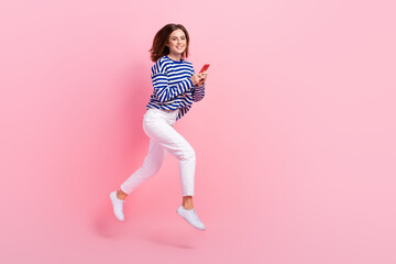 Full length photo of excited energetic person jumping rush hold use telephone isolated on pink color background