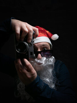 Santa in sunglasses taking pictures with a film camera on a dark background