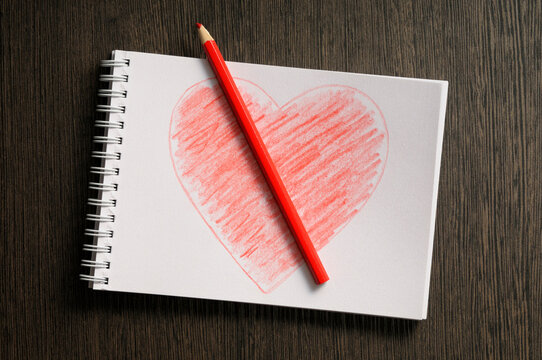 heart shaped drawing on notebook and colored pencil, wooden background, studio shot