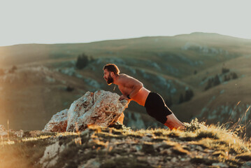 Muscular modern guy doing push-ups on top of mountain in nature