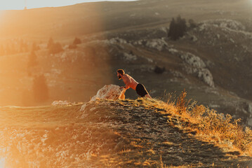 Muscular modern guy doing push-ups on top of mountain in nature