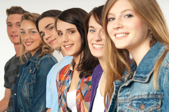 Close-up portrait of six, young men and young women in a row, smiling and looking at camera, studio shot on white background