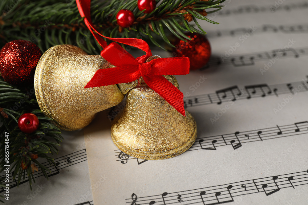 Poster Golden shiny bells and fir branches with Christmas decor on music sheets, closeup. Space for text